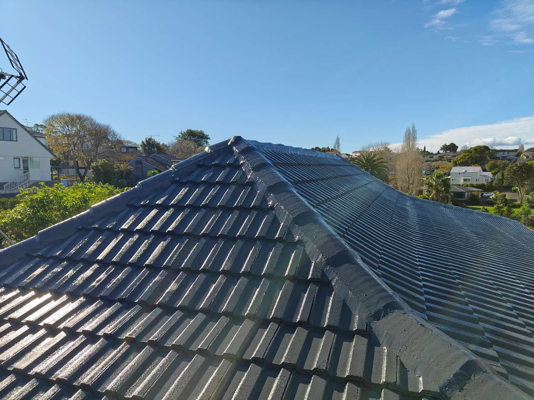 Auckland hip tile roof after full respray — even dark grey coating in bright sunlight with suburb backdrop