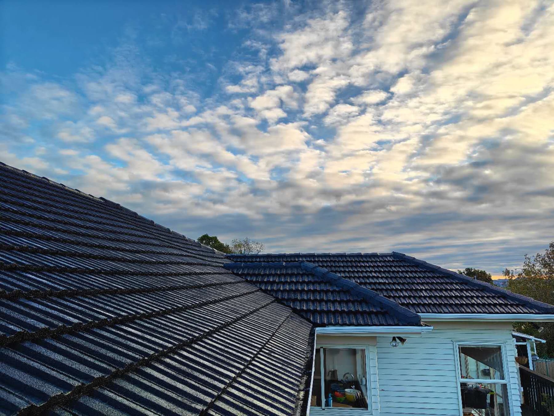 Freshly resprayed dark grey tile roof on an Auckland home, set against a dramatic cloud-streaked sky