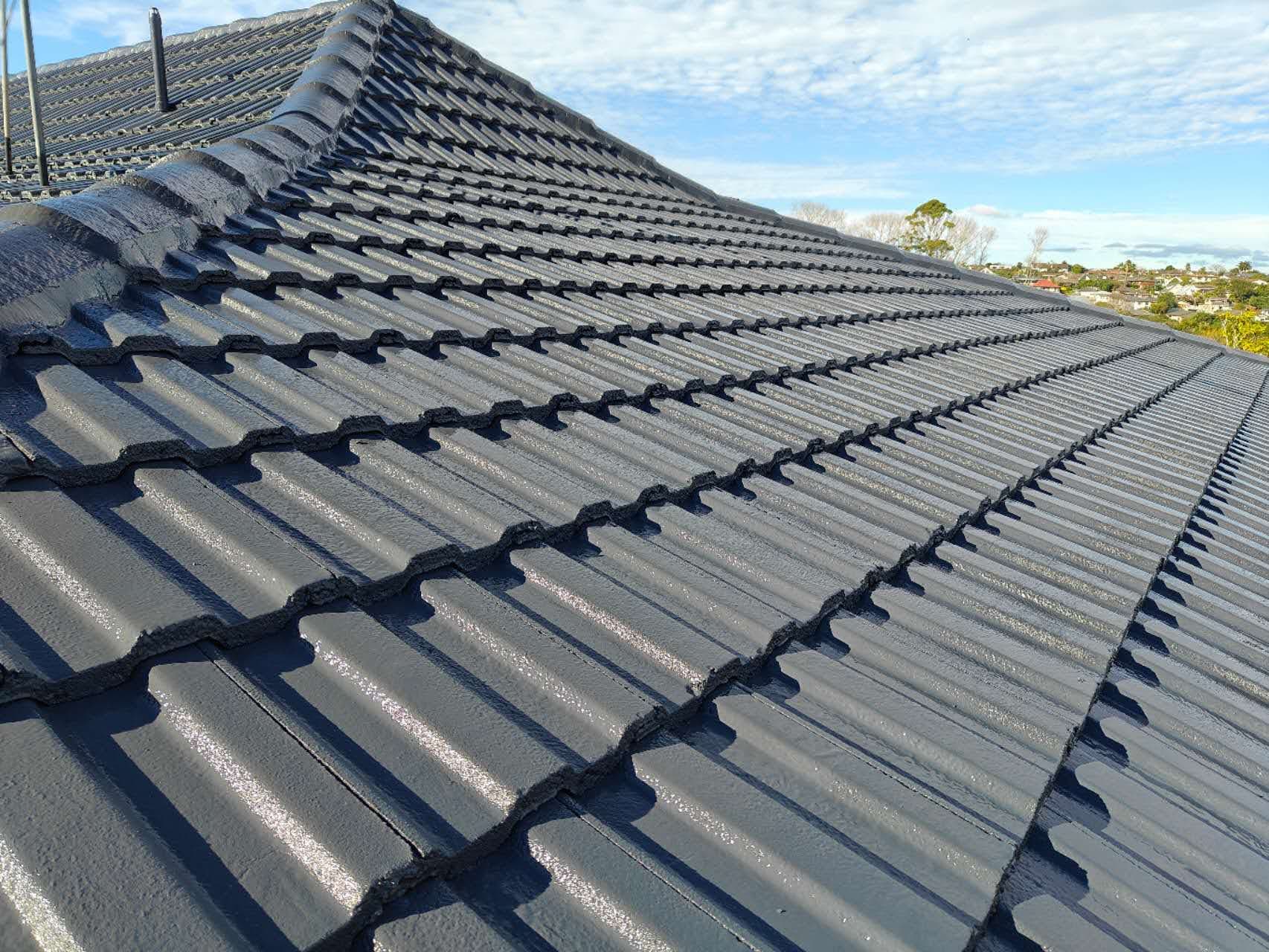 Close-up detail of freshly coated dark grey concrete tile roof against blue sky