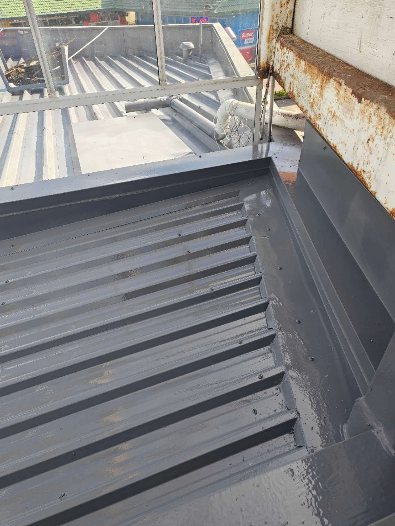 Commercial metal roof mid-respray — fresh grey coating applied to corrugated iron sheets